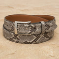 Handcrafted exotic python-print leather belt by Pellame Fino with a silver-tone buckle, coiled on a sandy beige surface